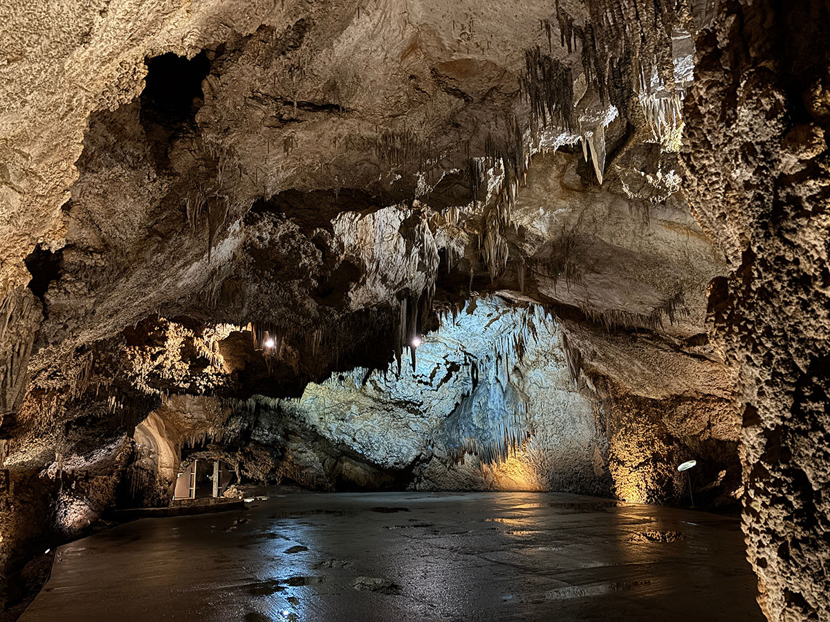 Beleuchtete Höhle mit niedrig hängenden Felswänden und von der Decke nach unten ragenden Formationen