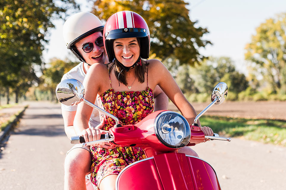 Zwei lachende junge Menschen auf einem Moped