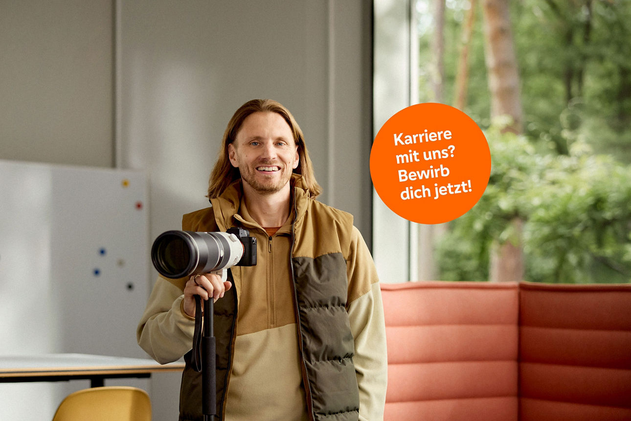 Ein Mann mit langen Haaren und einem breiten Lächeln hält eine Kamera in der Hand.