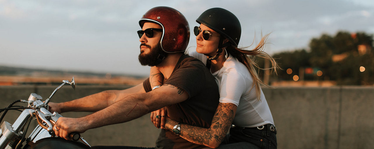 Mann und Frau fahren auf einem Motorrad in den Sonnenuntergang