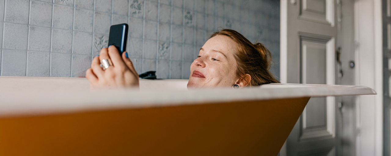 Eine Frau sitzt mit ihrem Handy in der Badewanne
