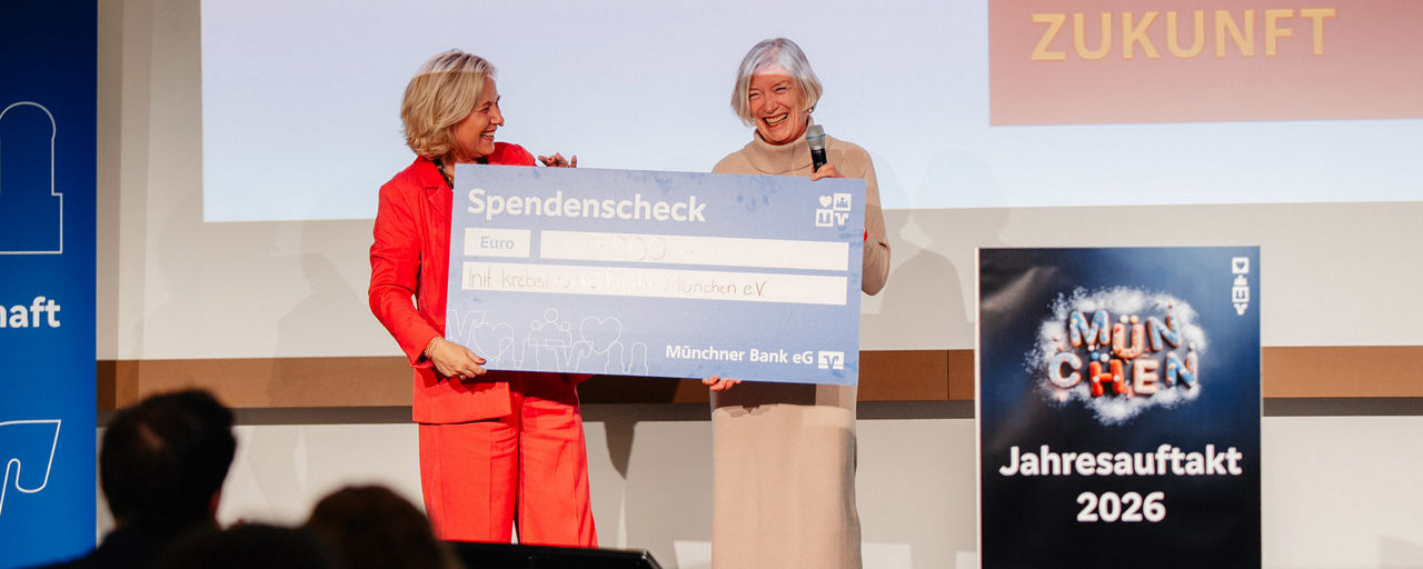 Eine Frau übergibt einer anderen Frau einen Spendenscheck