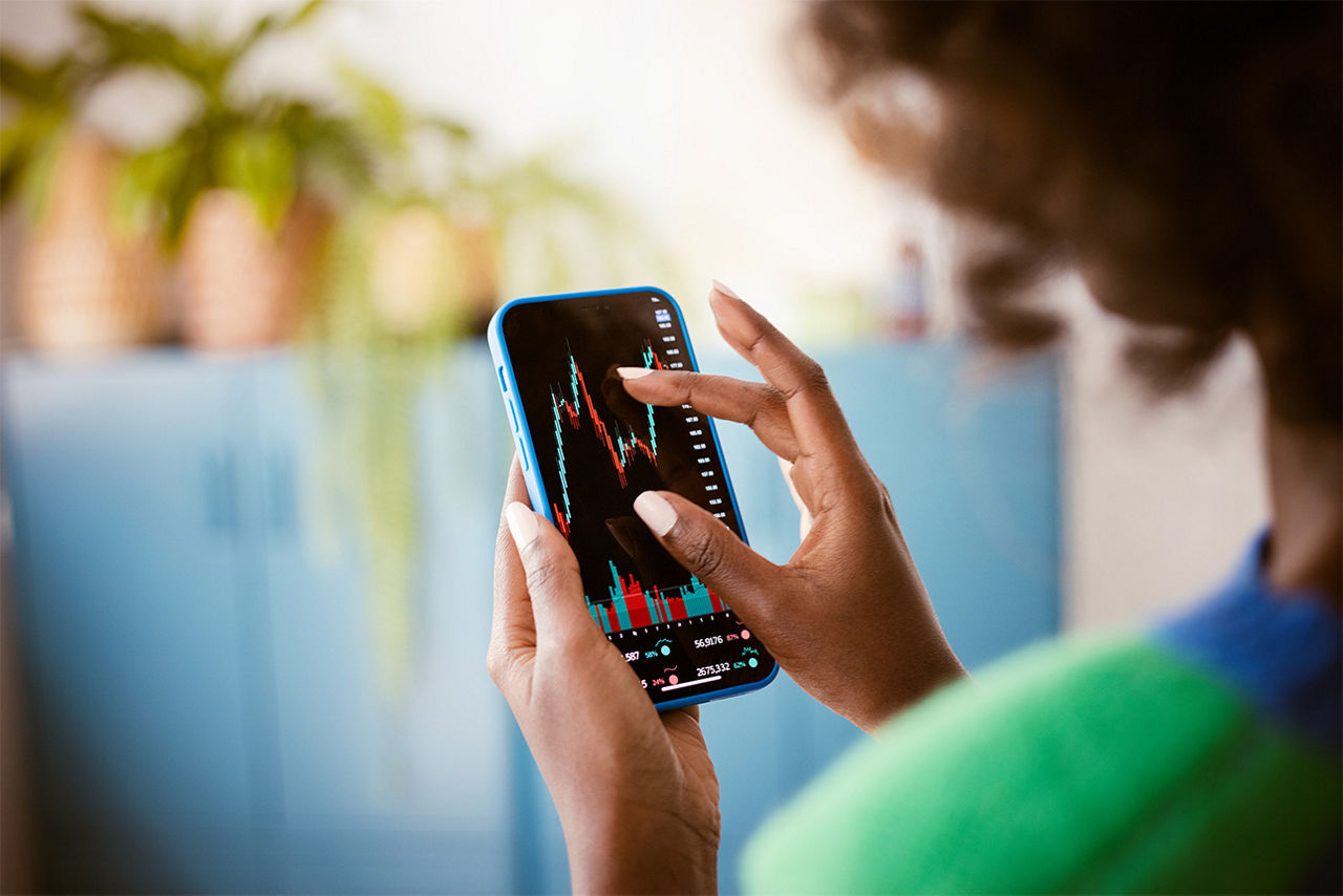 Frau schaut auf einen Börsengraphen auf ihrem Smartphone.