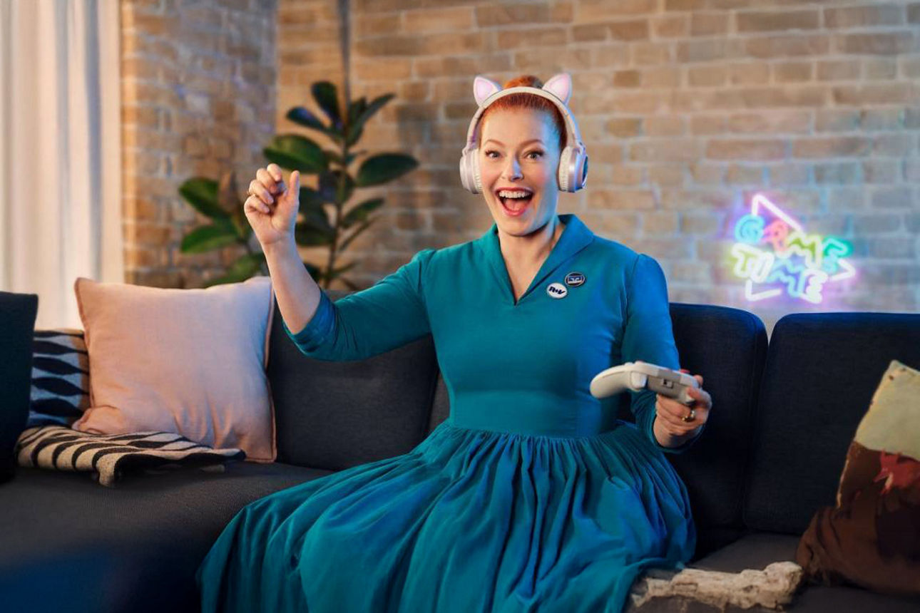 Eine junge Frau sitzt mit einem Controller auf einer Couch