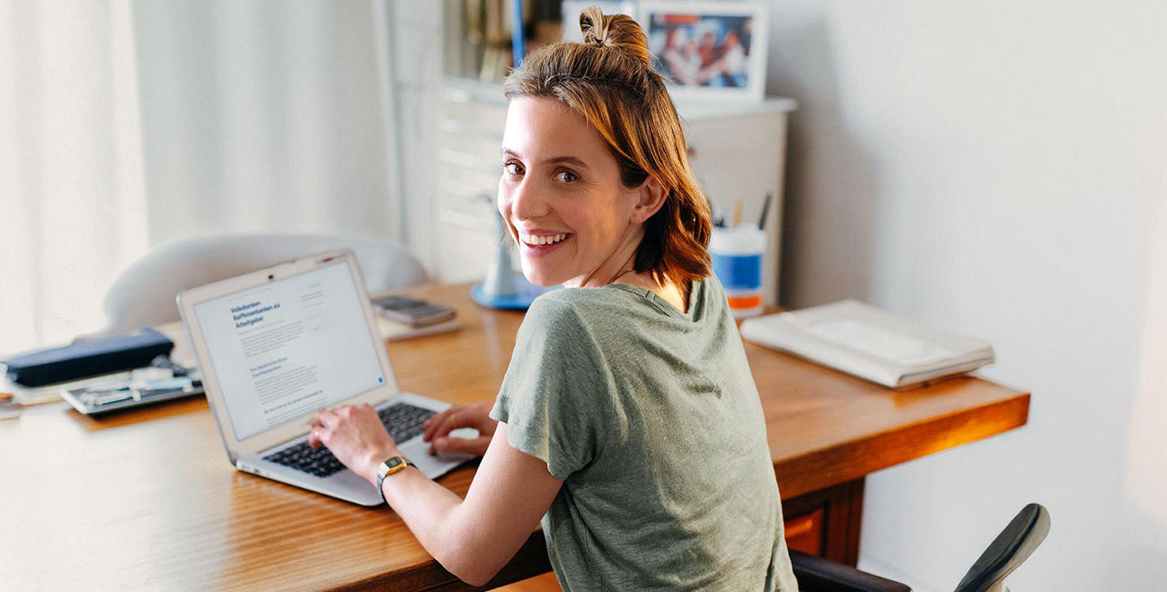 Eine junge Frau sitzt an einem Tisch vor Ihrem Laptop