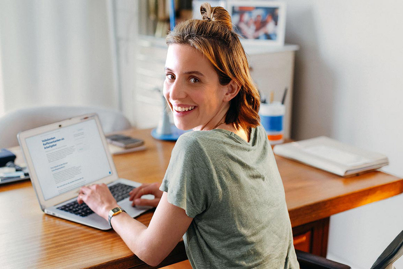 Eine junge Frau sitzt an einem Tisch vor Ihrem Laptop