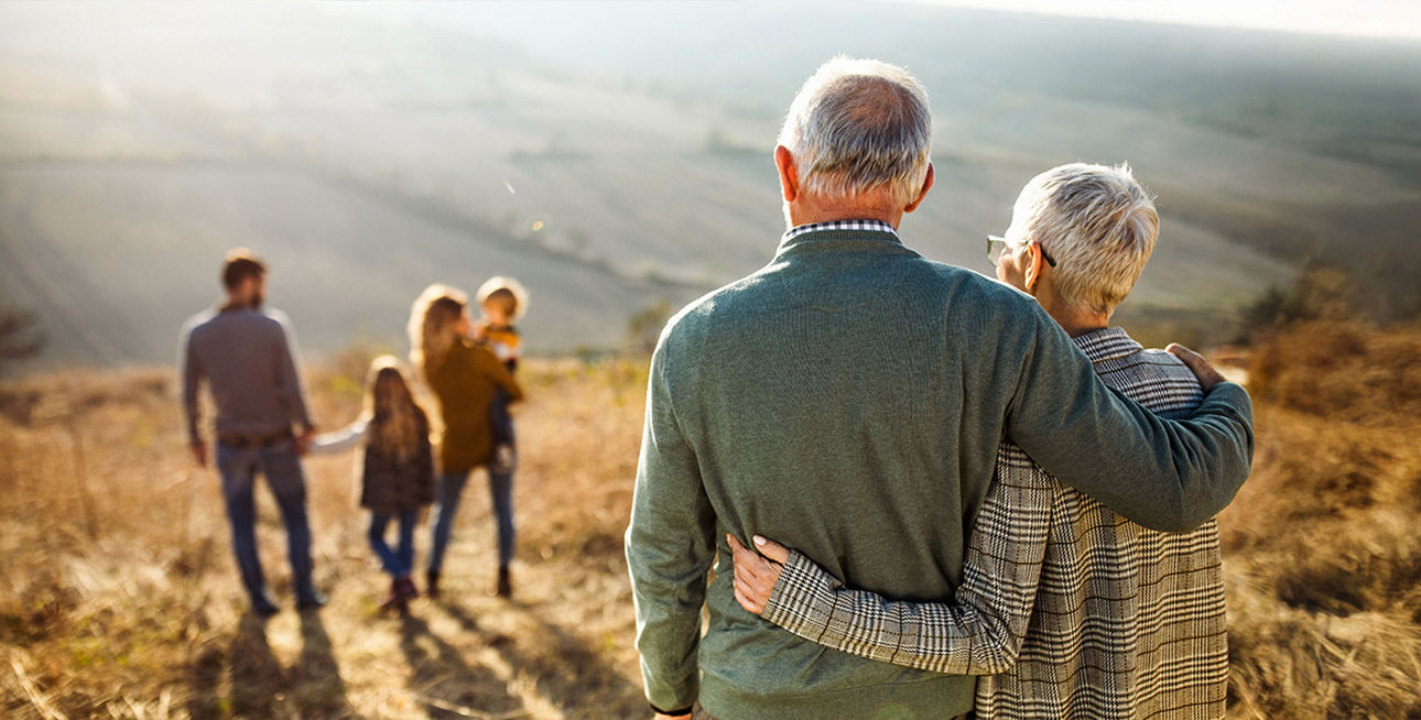 Ein älteres Paar umarmt sich auf einem Feld und schaut auf ihre Familie