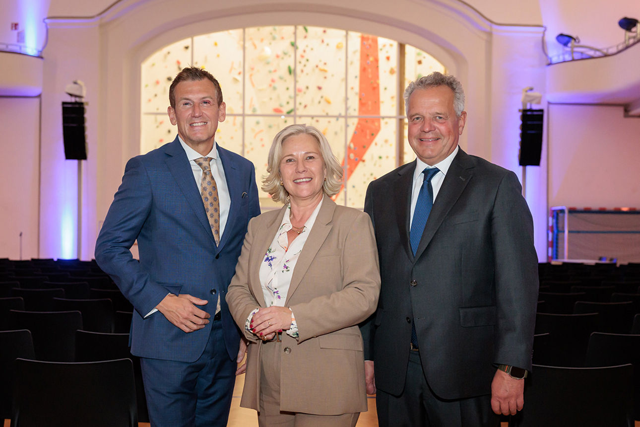 Zwei Männer und eine Frau stehen lächelnd nebeneinander