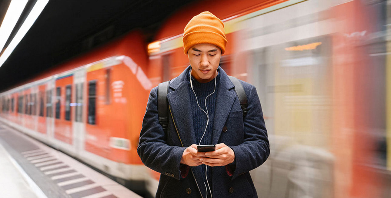 Mann in einer U-Bahn-Station, der auf sein Smartphone schaut