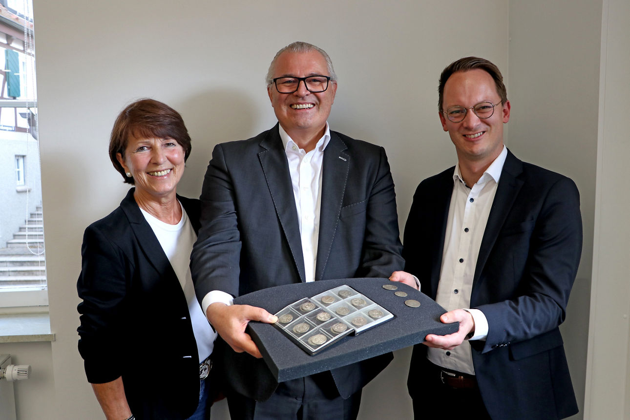 Co-Vorstandssprecher Jörg Stahl steht mit Hilde Aichele neben Herrenbergs Oberbürgermeister Nico Reith und übergbit Münzfund.