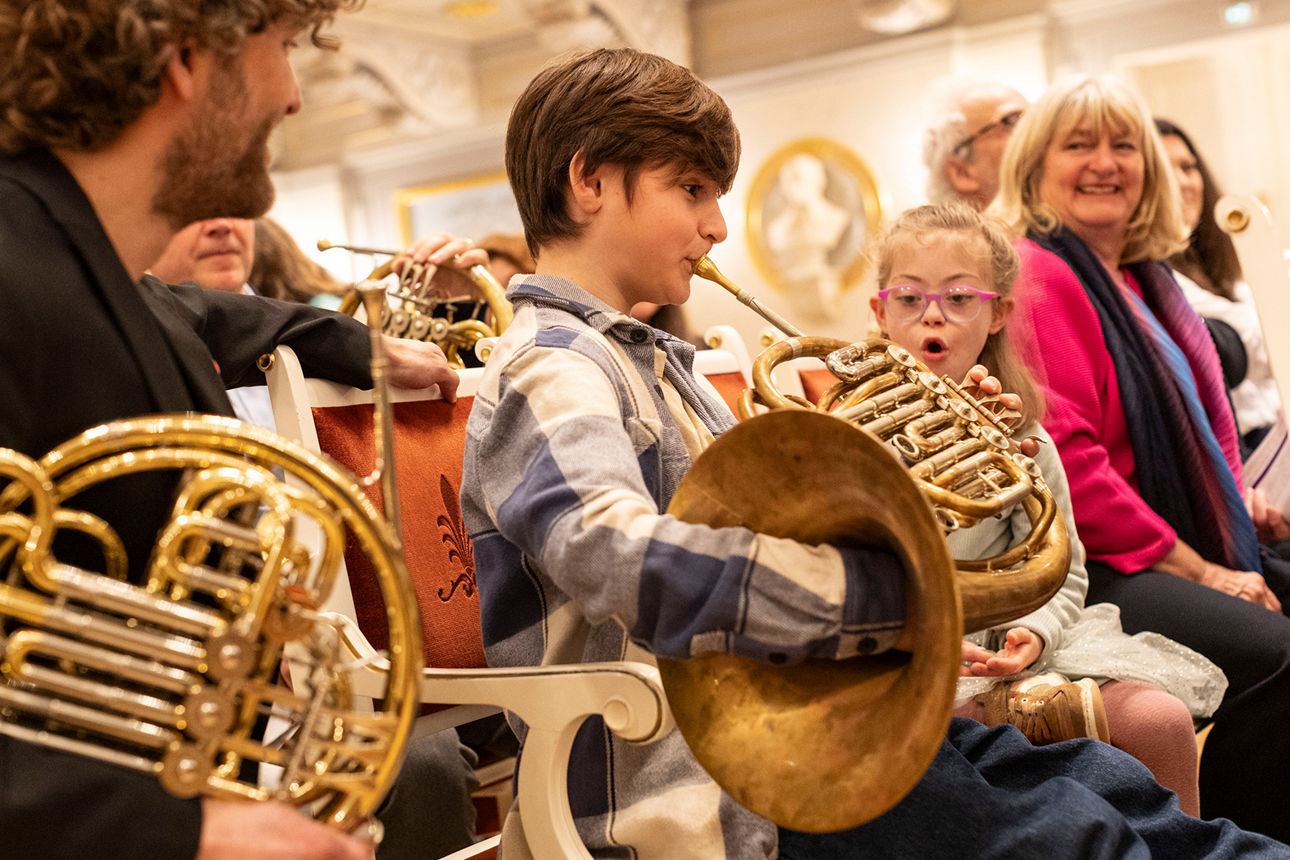 Ein Junge spielt auf einem Horn und ein Mädchen schaut begeistert zu