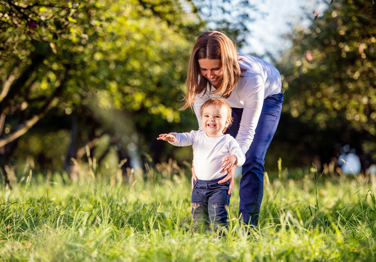 Mutter lernt ihrem kleinen Kind im grünen Garten laufen