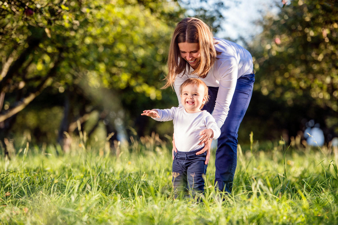 Mutter lernt ihrem kleinen Kind im grünen Garten laufen