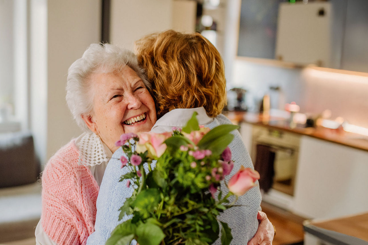 Zwei Frauen umarmen sich und halten dabei einen Blumenstrauß