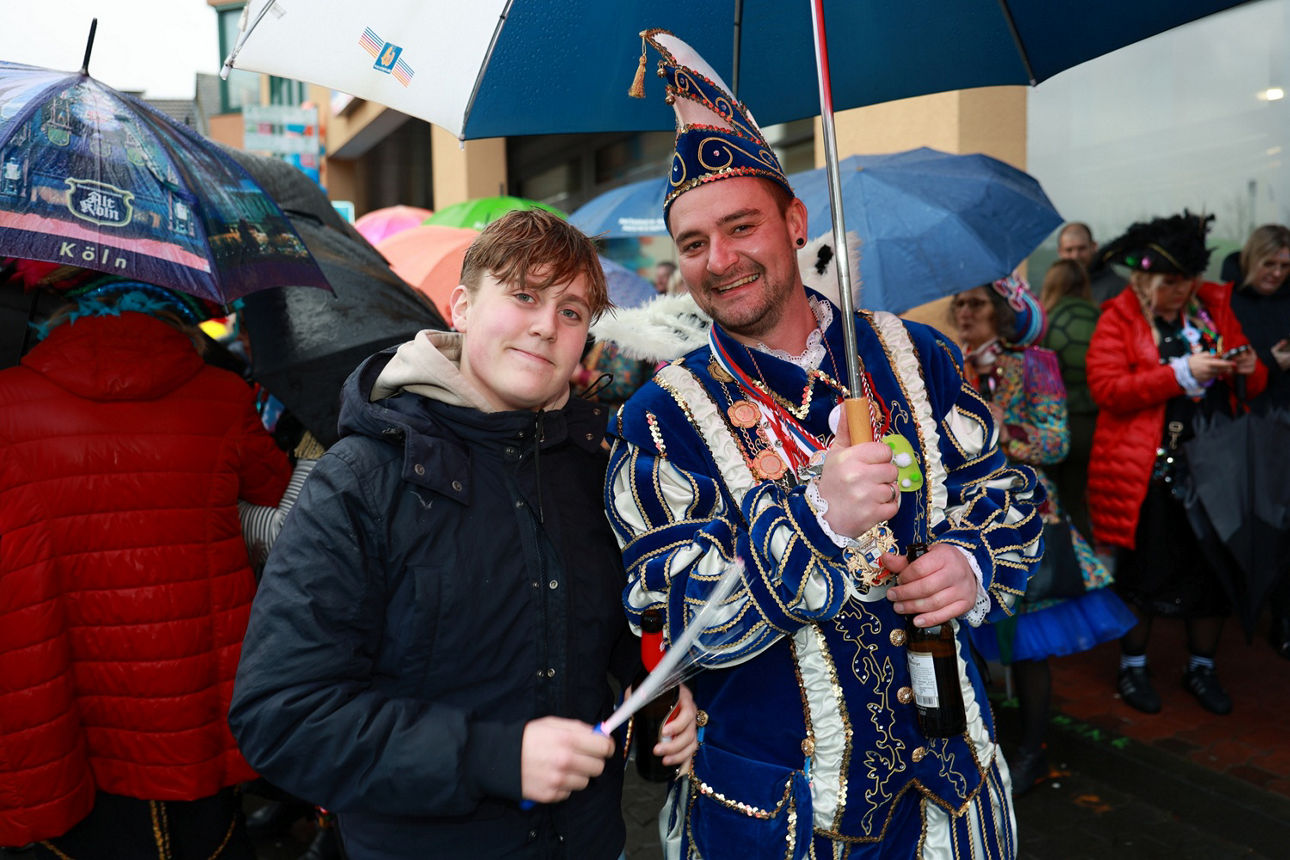 Der Kinderprinz der letzten Session mit Leuchtstab neben dem aktuellen Prinzen in blau-weißem Gewand unter einem Regenschirm