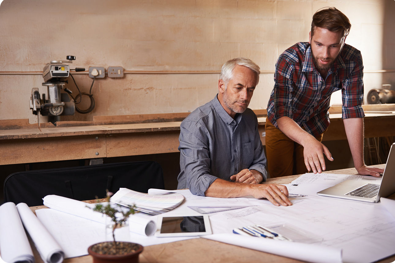Ein älterer Mann sitzt mit einem jüngeren Mann an einer Werkbank