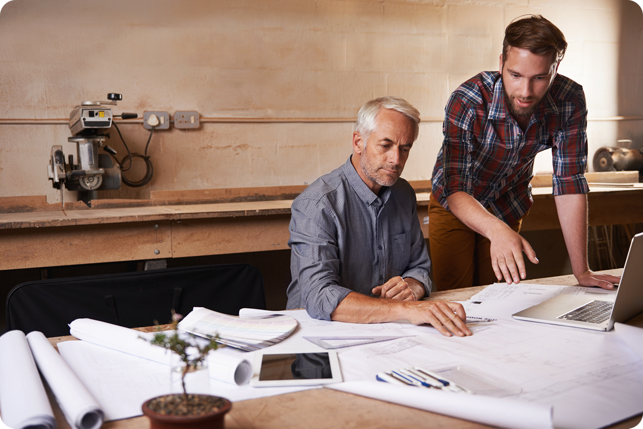 Ein älterer Mann sitzt mit einem jüngeren Mann an einer Werkbank