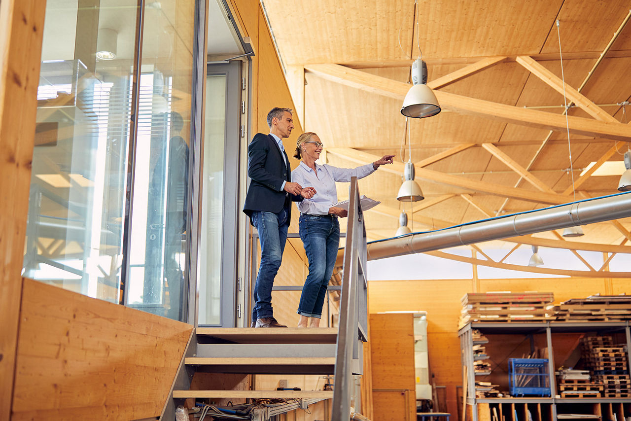 Geschäftsführerin steht auf einer Treppe vor ihrem Büro und zeigt in die Werkstatthalle