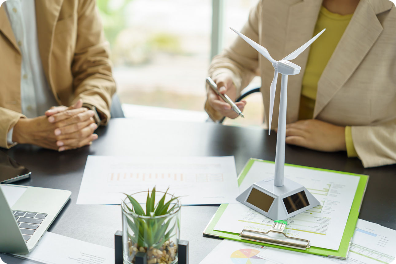 Eine Frau und ein Mann sitzen an einem Schreibtisch. Darauf steht ein Miniaturwindrad.