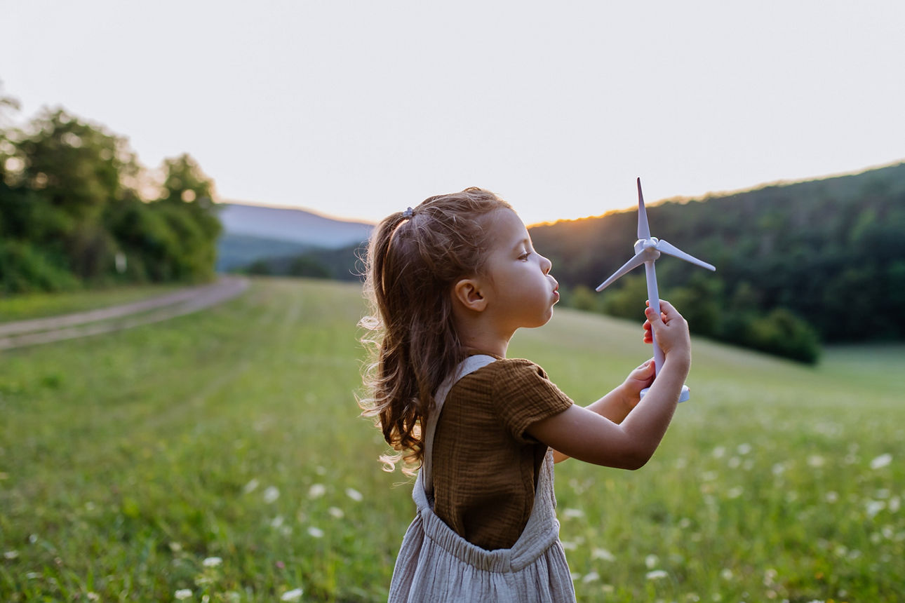 Ein kleines Mädchen auf einer blühenden Wiese bläst ein kleines Windrad