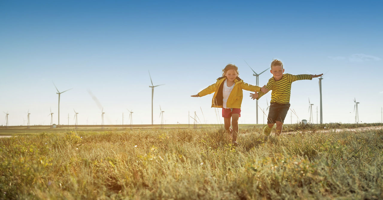 Kinder rennen auf einer Wiese im Hintergrund sind Windkaftanlagen