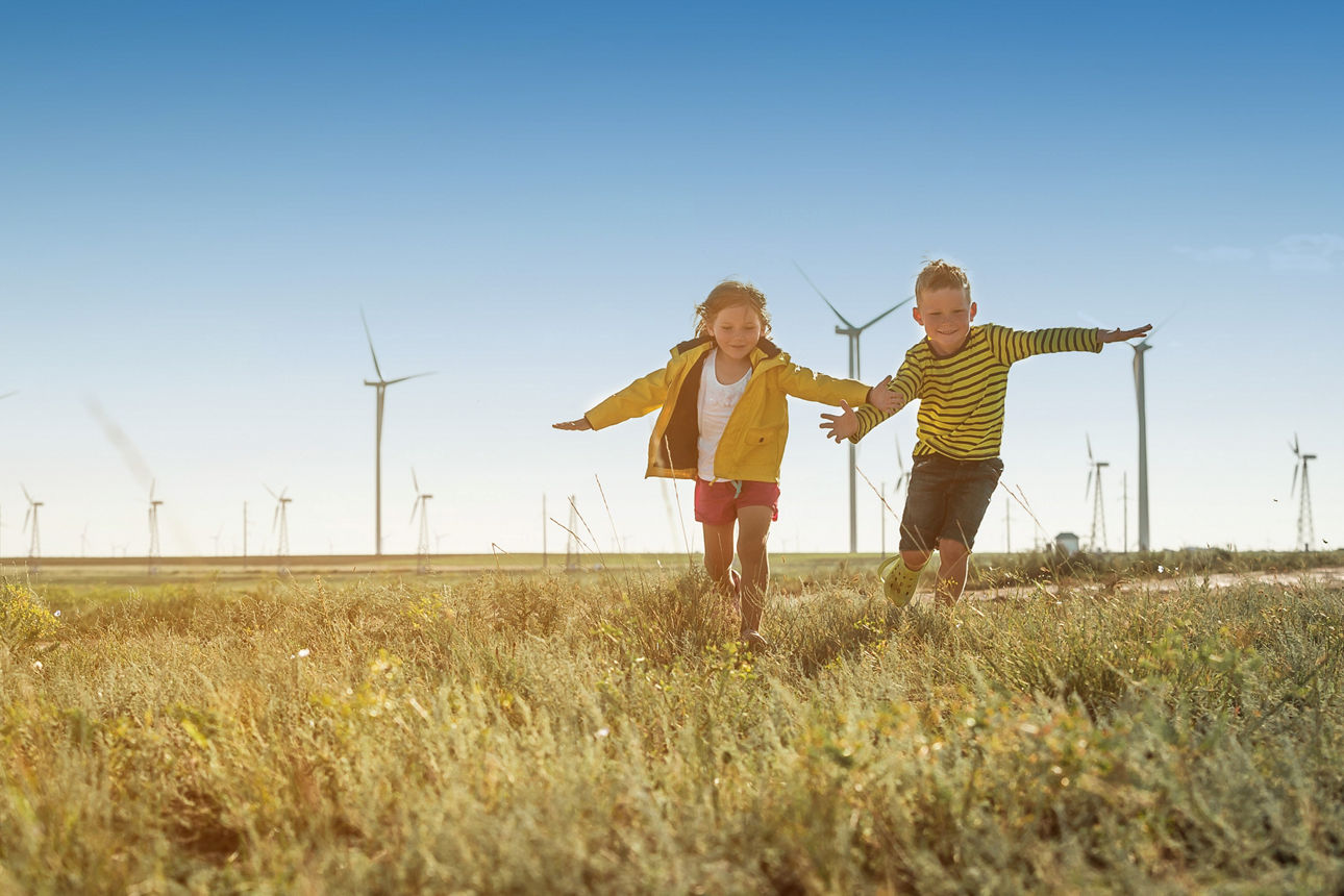 Kinder rennen auf einer Wiese im Hintergrund sind Windkaftanlagen