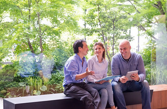Drei Kollegen sitzen im Büro vor einer Glasfront die den Blick auf viel Grün draußen ermöglicht