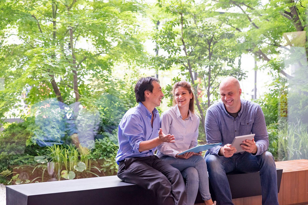 Drei Kollegen sitzen im Büro vor einer Glasfront die den Blick auf viel Grün draußen ermöglicht