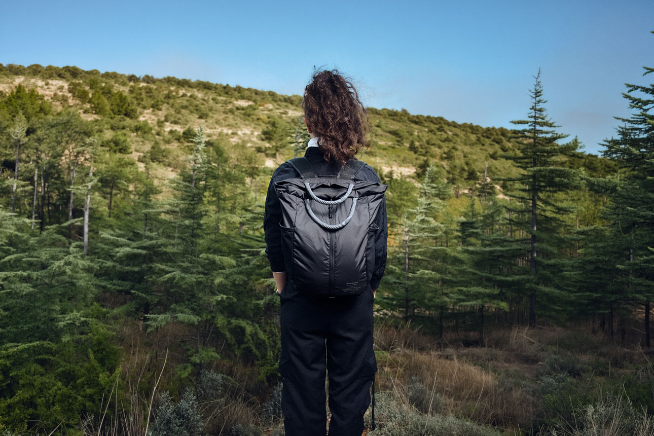 Nachhaltigkeit trifft Innovation: Wie Ucon Acrobatics die Fashionbranche neu denkt Person mit Rucksack blickt auf bewaldete Hügellandschaft.