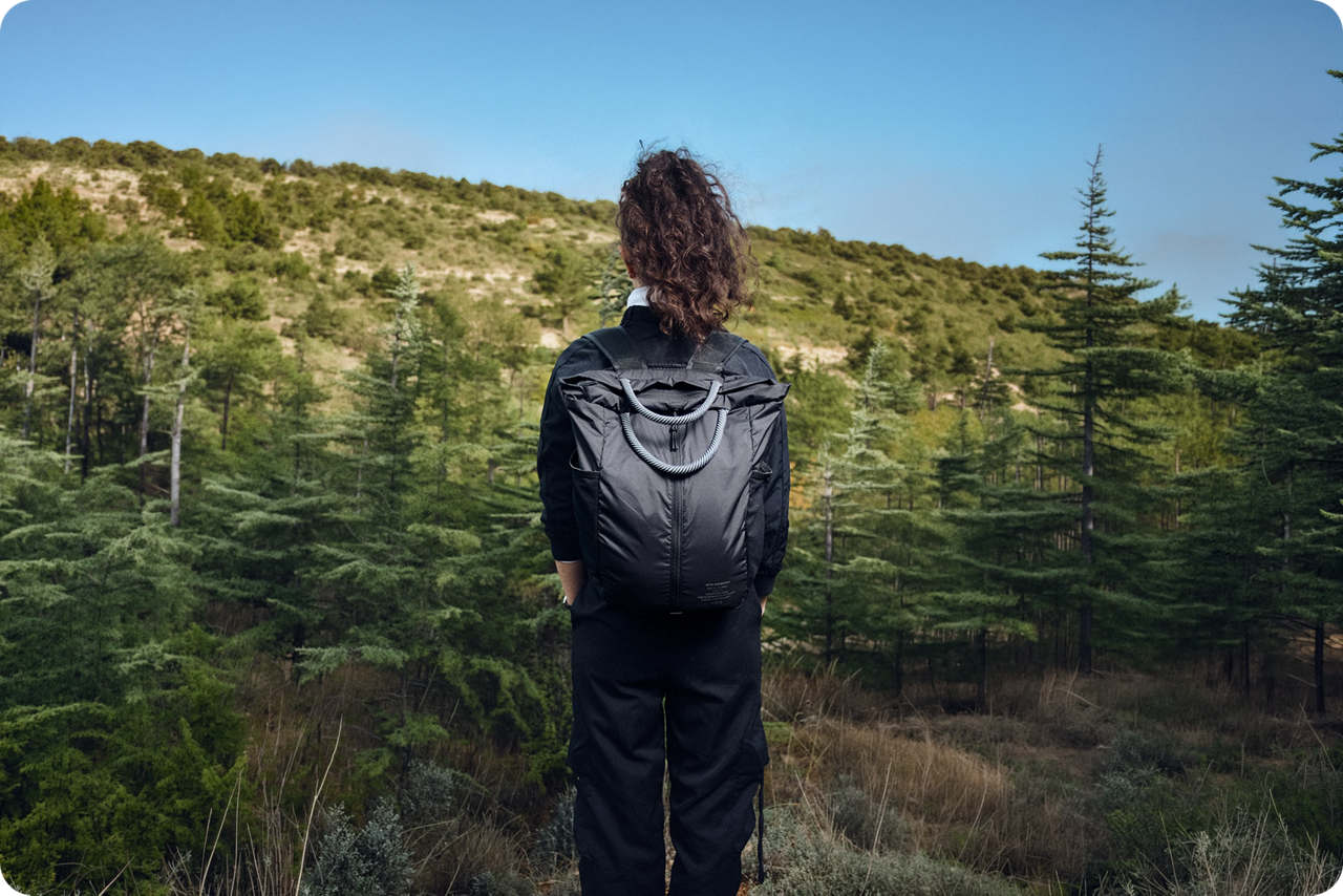 Person mit Rucksack blickt auf bewaldete Hügellandschaft.