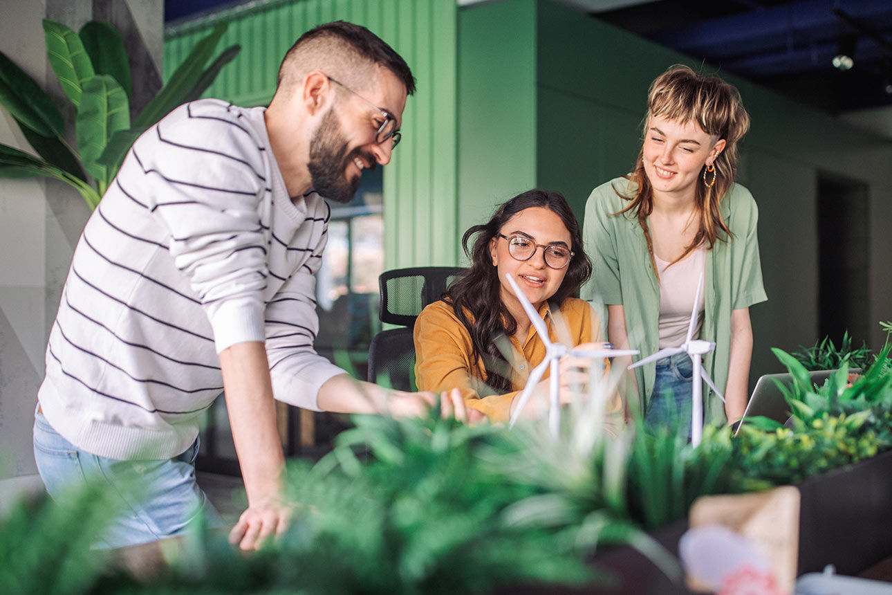 Drei junge Menschen stehen an einem Schreibtisch mit Windrad-Modellen und einigen Pflanzen