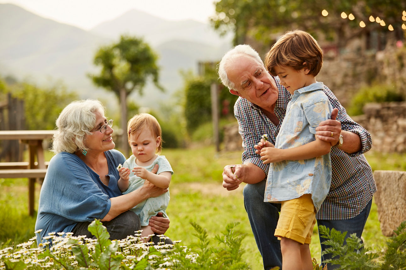 Großeltern sprechen mit Kindern. Die Familie verbringt die Freizeit im Garten. Sie tragen Freizeitkleidung.