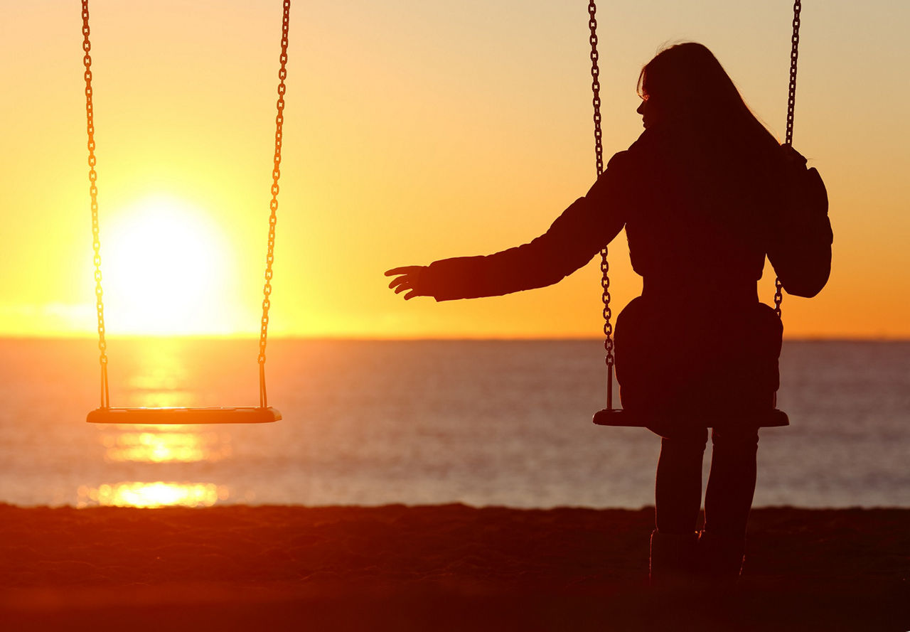 Eine Frau sitzt auf einer Schaukel vor einem Sonnenuntergang