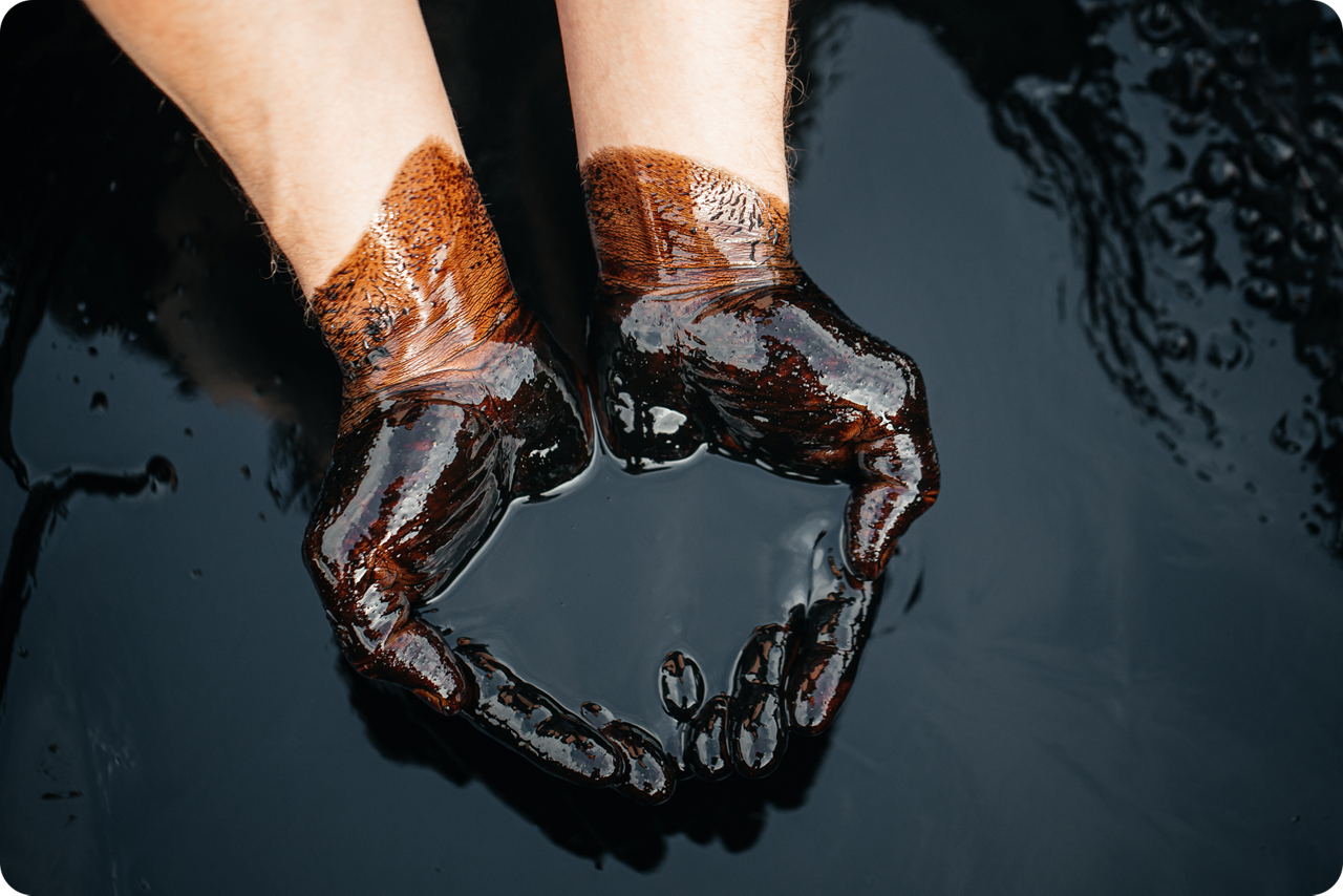 Zwei Hände, mit schwarzem Öl verschmutzt, formen eine Schale und halten eine kleine Menge Flüssigkeit.