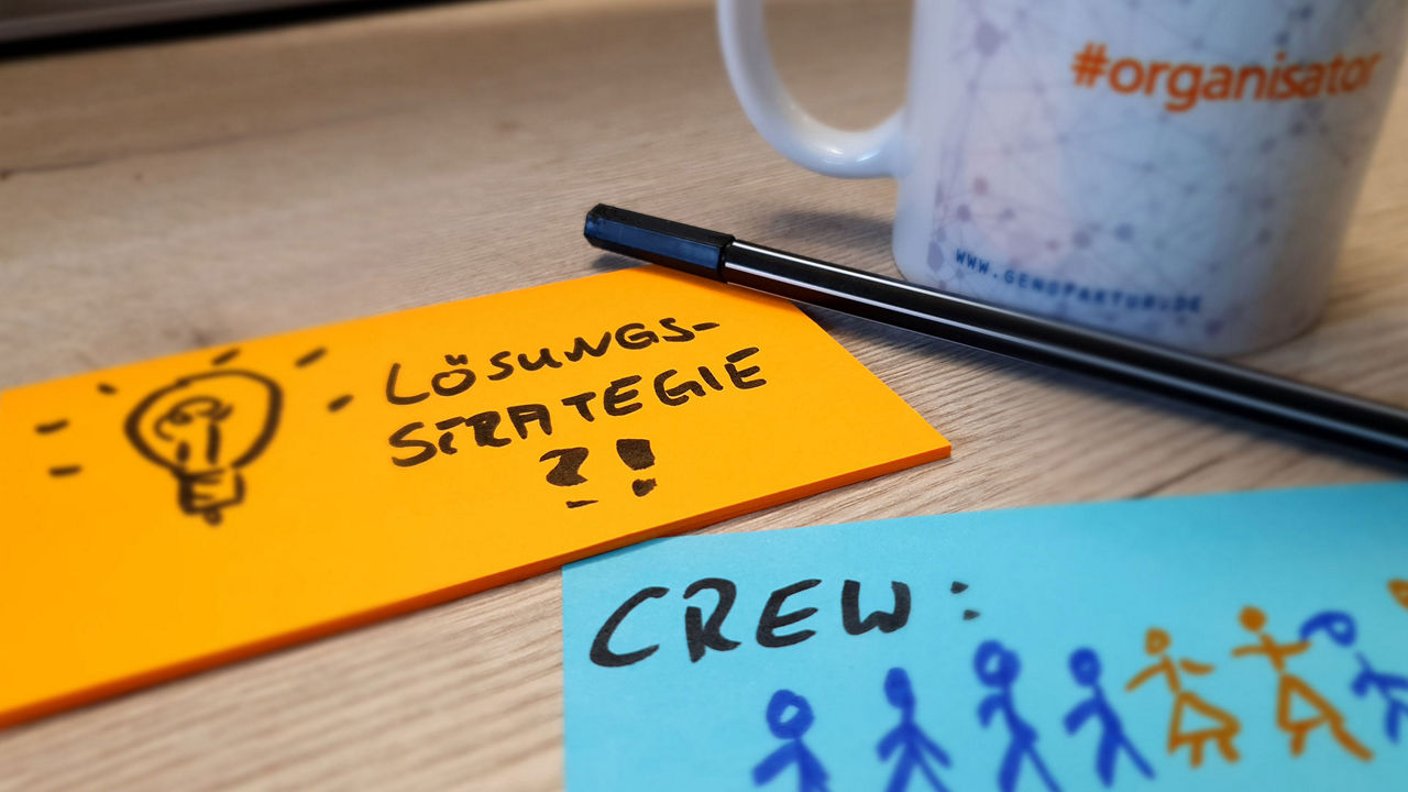 Zwei kleine Notizblöcke, eine Tasse und ein Stift liegen auf einem Tisch