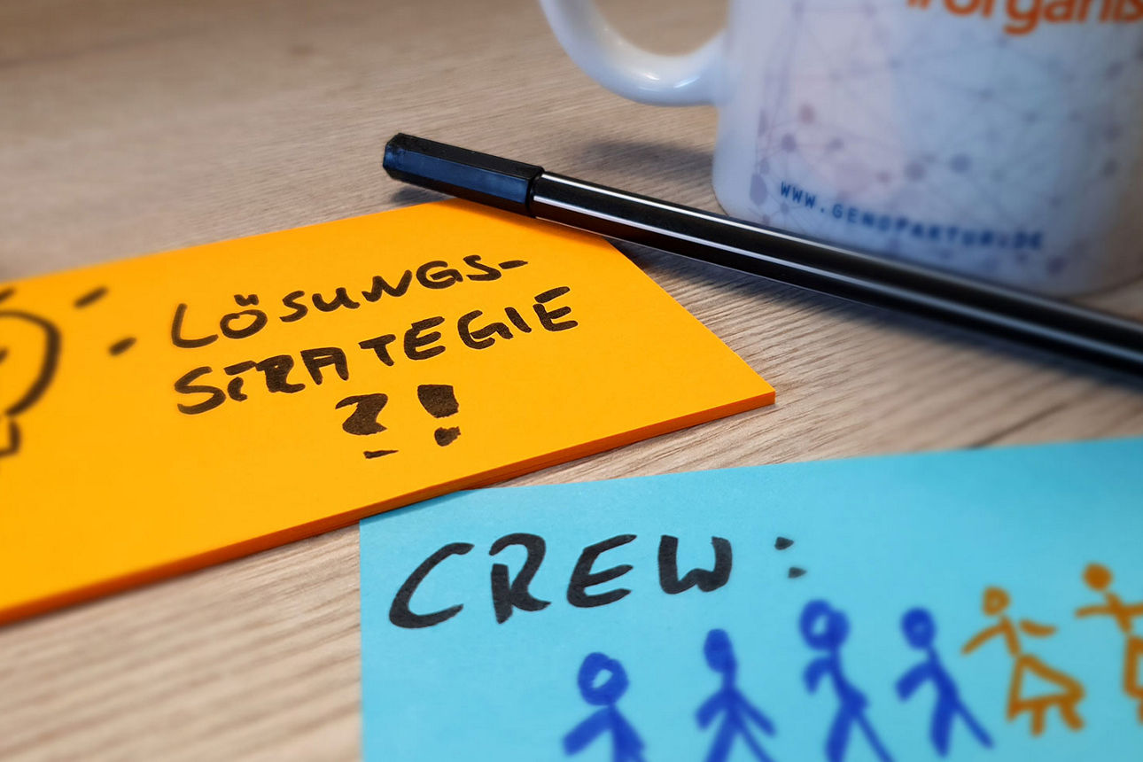 Zwei kleine Notizblöcke, eine Tasse und ein Stift liegen auf einem Tisch