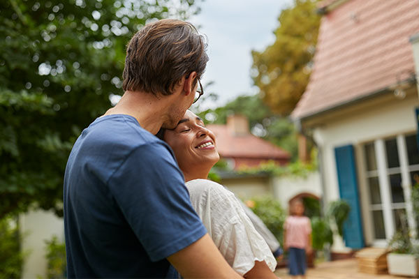 Mann und Frau umarmen sich sichtbar glücklich vor Ihrem neuen Traumhaus.