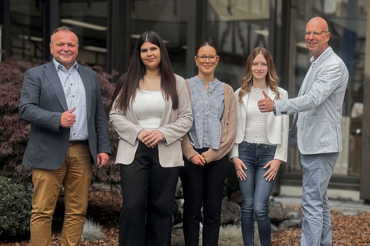 Neue Azubis, die schick gekleidet sind, mit zwei Männern, die den Daumen hochhalten.