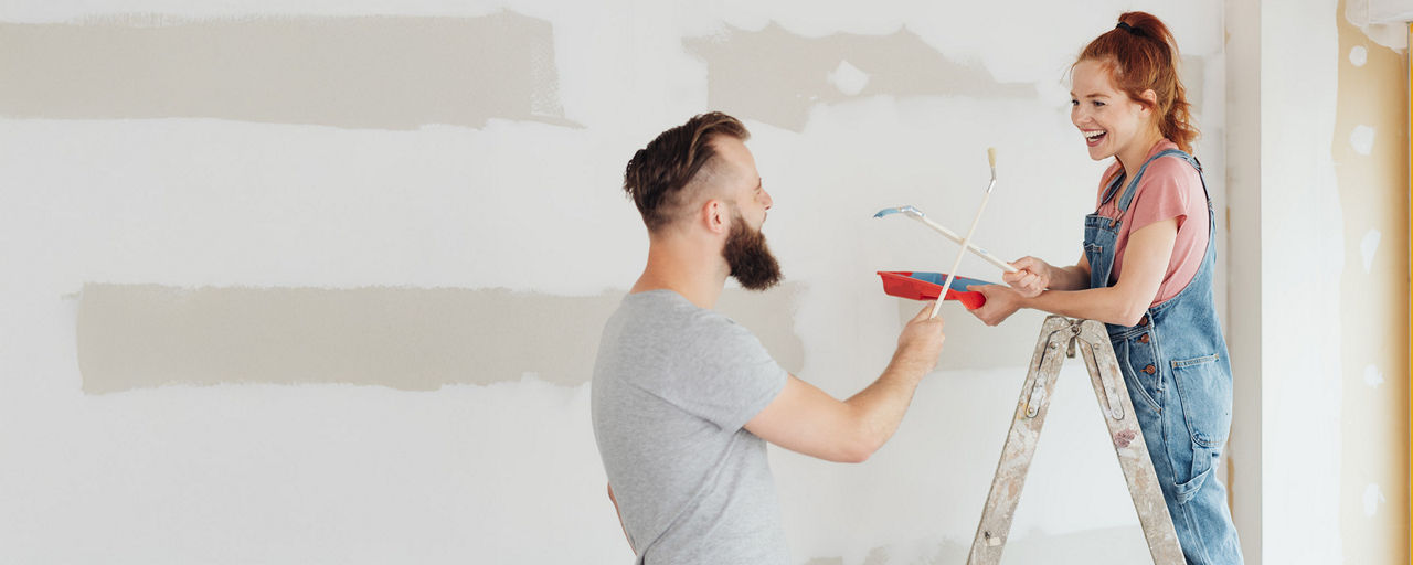 Junges Pärchen streicht lachend eine Wand in der neuen Wohnung