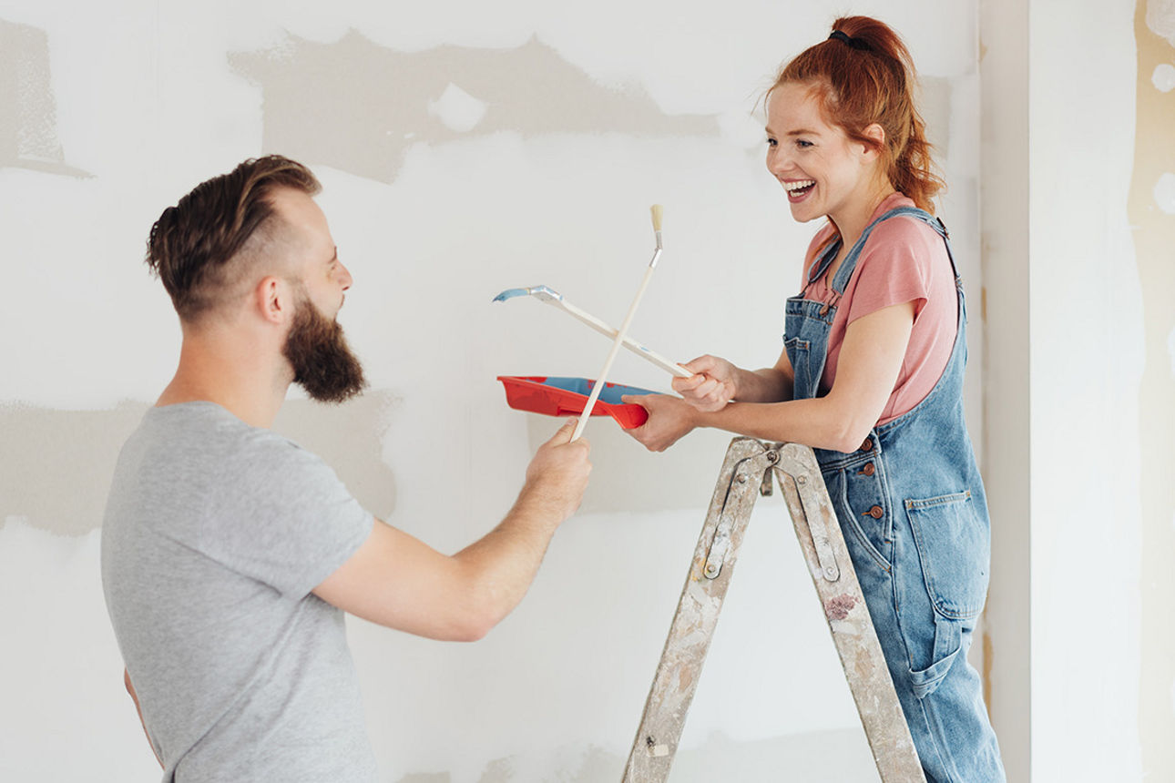 Junges Pärchen streicht lachend eine Wand in der neuen Wohnung