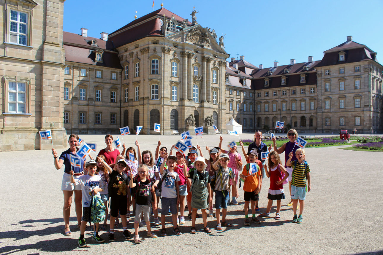 Kinder stehen mit Raiffeisenbank-Fahnen vor dem Schloss Pommersfelden.