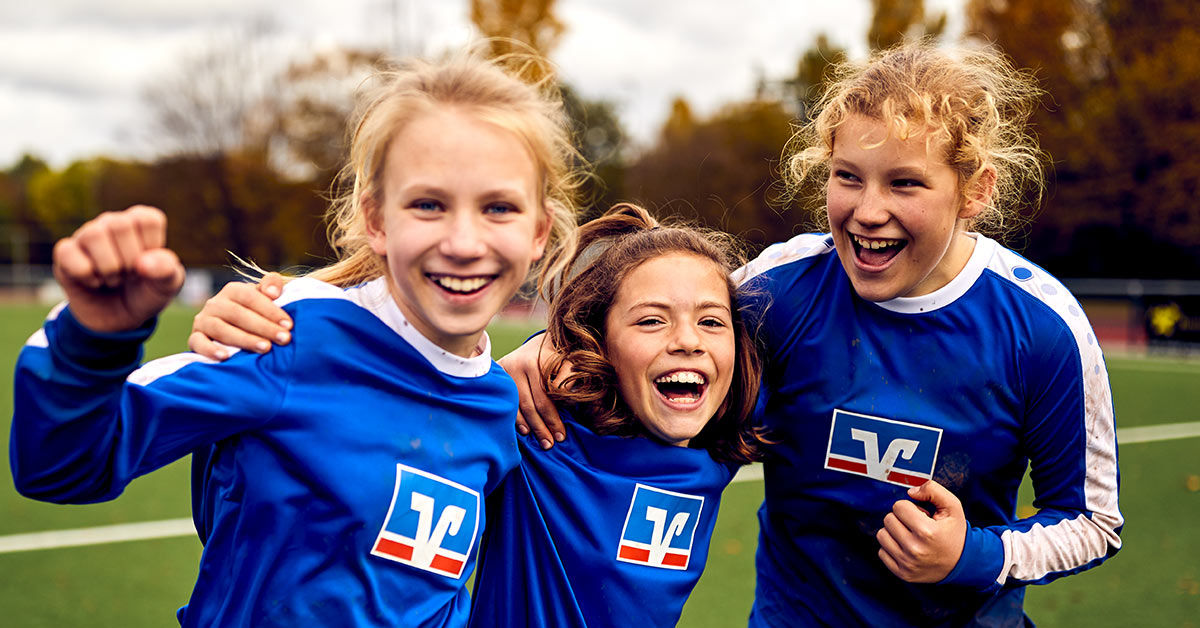 Drei Kinder einer Fußballmannschaft in Volksbank-Trikots freuen sich über ihren Erfolg