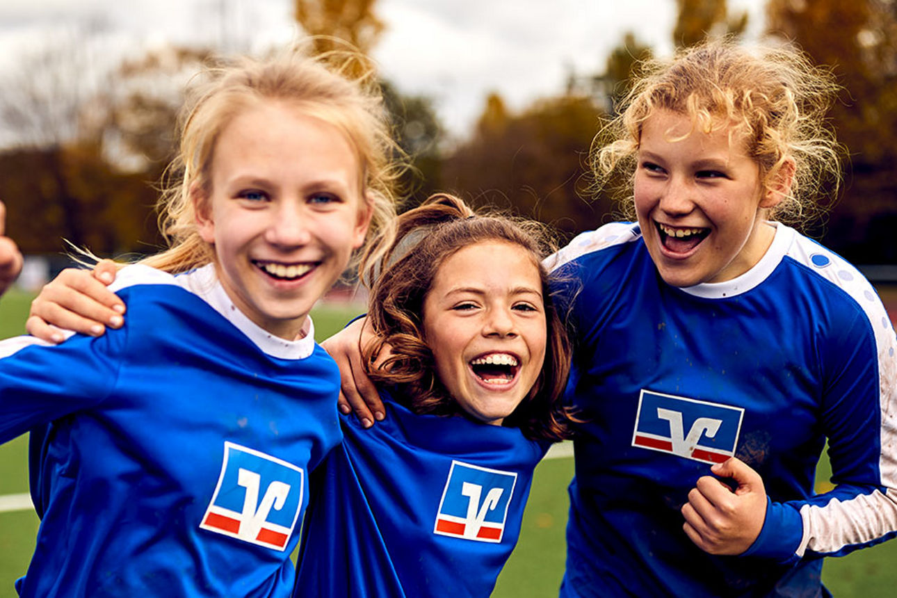 Drei Kinder einer Fußballmannschaft in Volksbank-Trikots freuen sich über ihren Erfolg