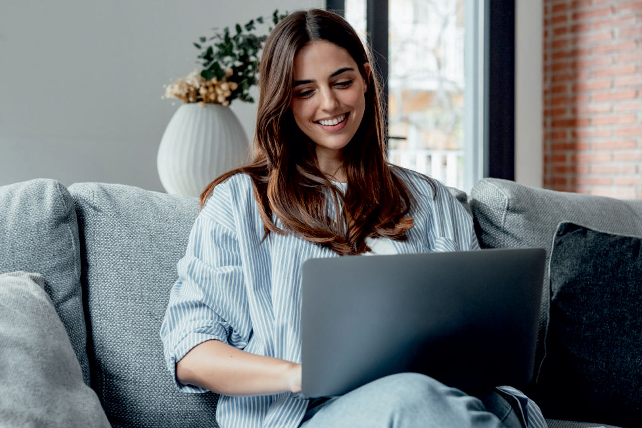 Eine junge Frau sitzt auf der Couch und arbeitet am Laptop