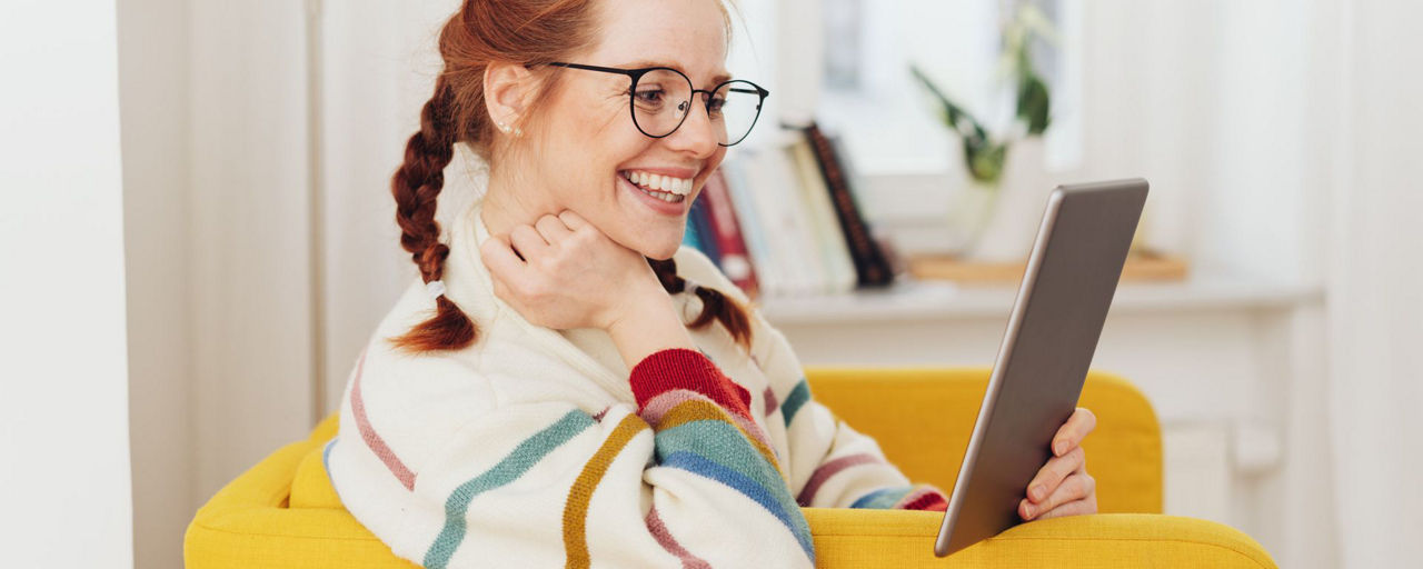 Frau schaut lachend auf einen Tablet PC