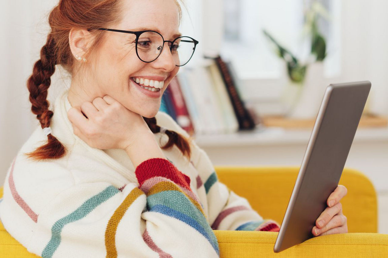 Frau schaut lachend auf einen Tablet PC