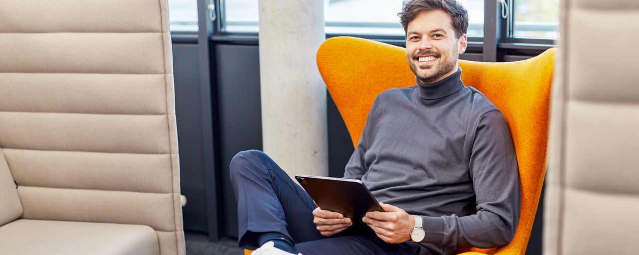Lächelnder Mann sitzt mit einem Tablet auf einem Stuhl