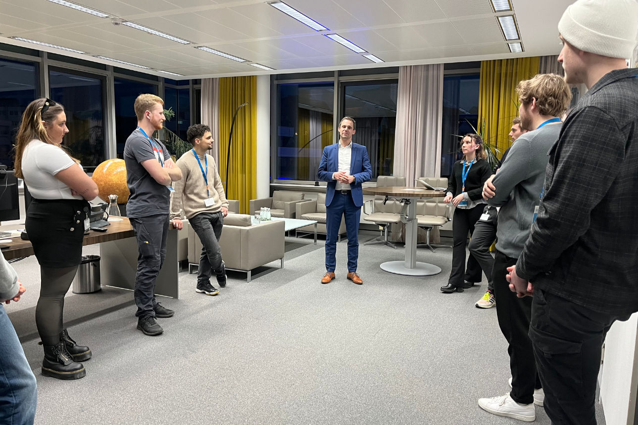 Person spricht vor einer Gruppe in einem modernen Besprechungsraum mit großen Fenstern.