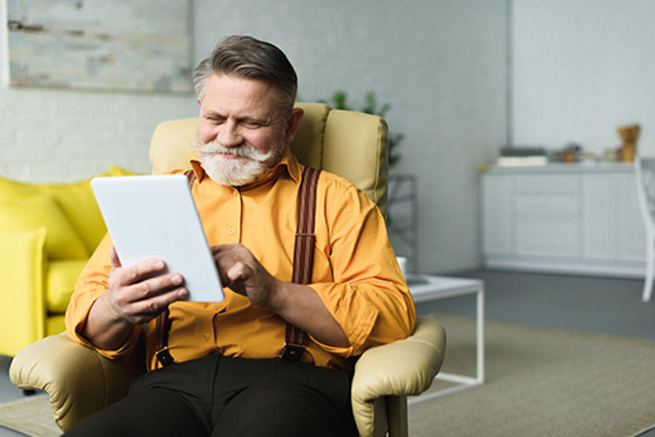 Älterer Herr sitzt mit einem Tablet in einem Sessel