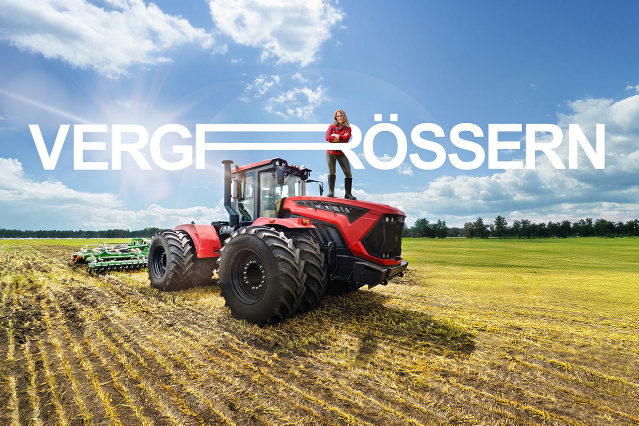 Eine Landwirtin posiert mit verschränkten Armen auf einem großen Traktor, der mitten auf einem Acker steht